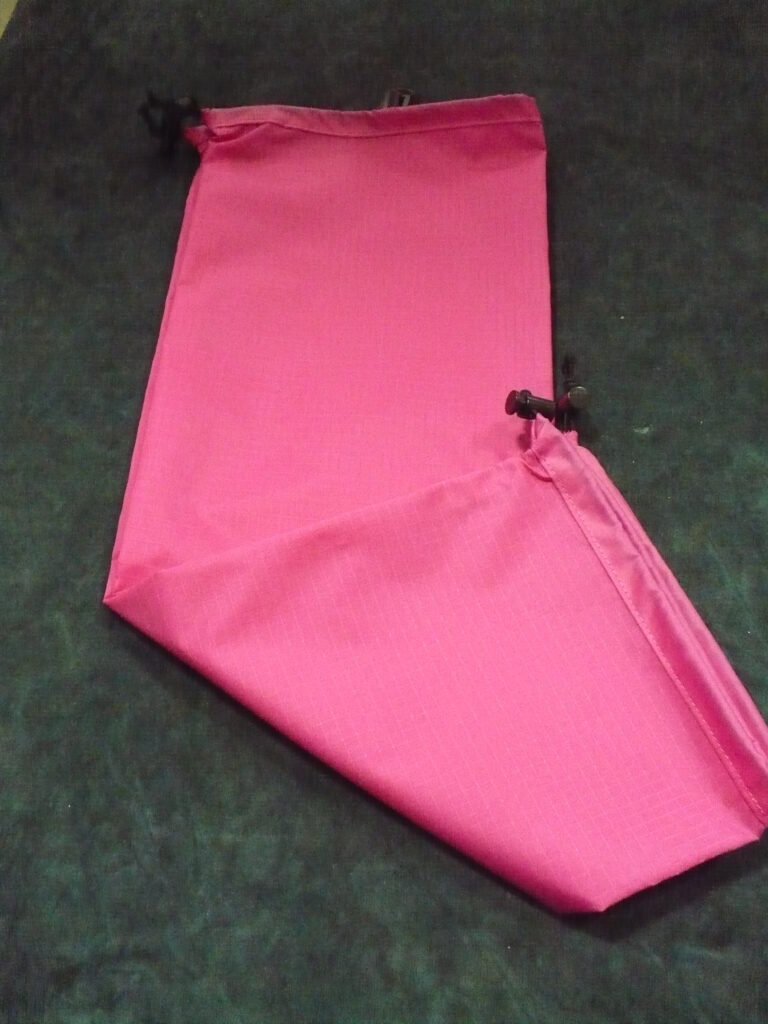 Bright pink fabric sleeve with a drawstring closure on a dark surface